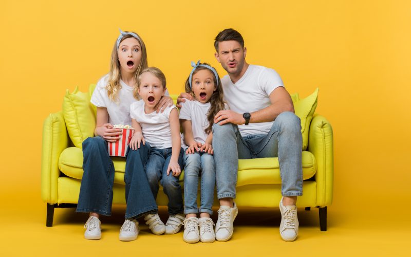 shocked family watching movie on sofa with popcorn bucket on yellow